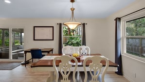 Un comedor con mesa de madera, sillas blancas y una araña.