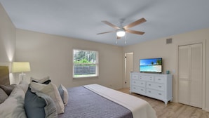 Un dormitorio con cama, cómoda, televisor y ventilador de techo.