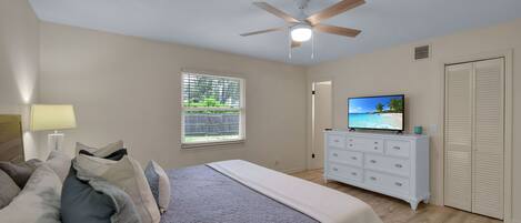 A bedroom with a bed, a dresser, a television, and a ceiling fan.