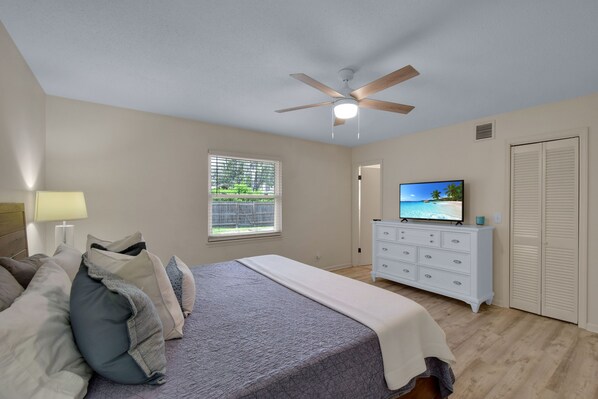 A bedroom with a bed, a dresser, a television, and a ceiling fan.