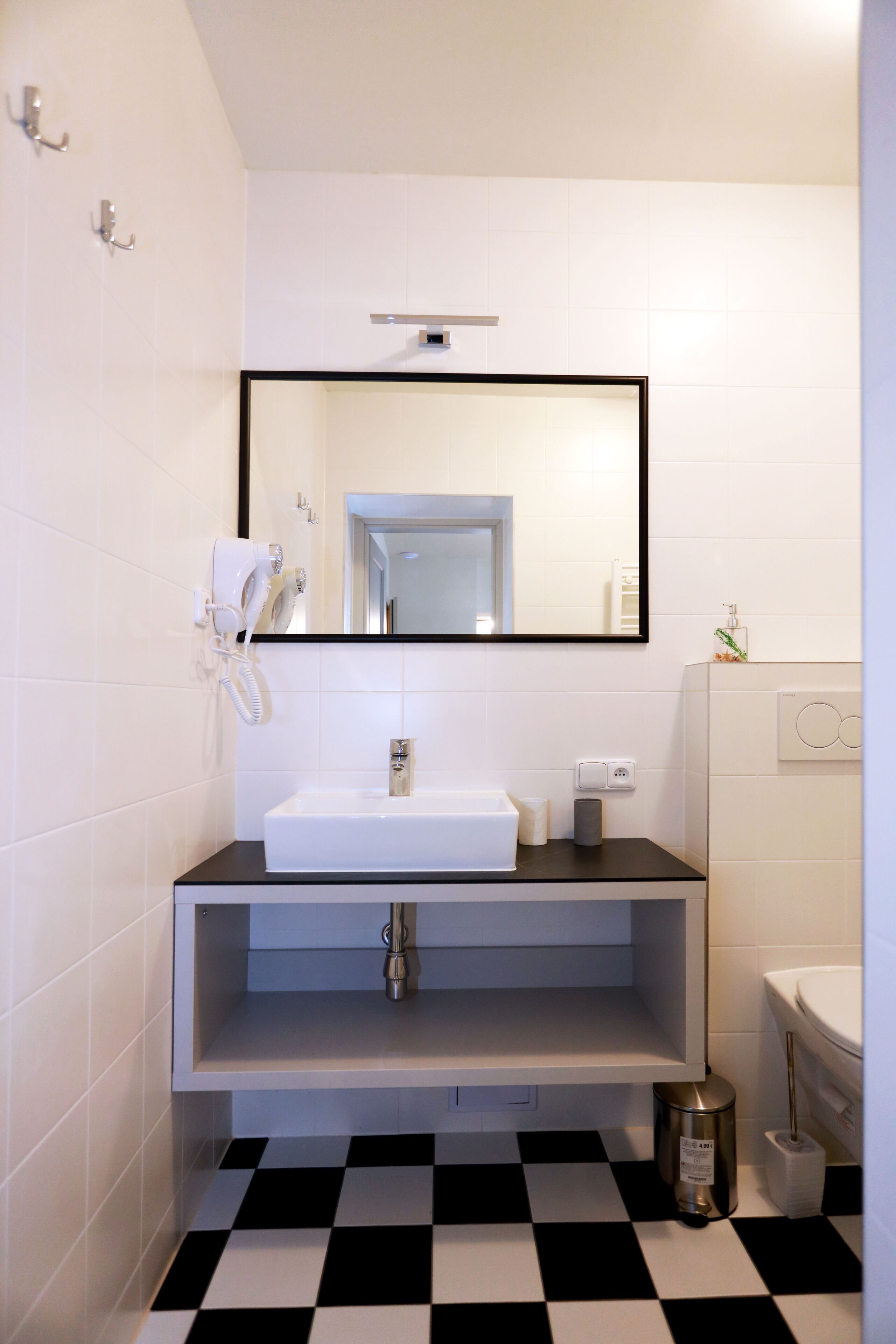 A bathroom with a black and white checkered floor, a white sink, a mirror, and a hairdryer mounted on the wall.
