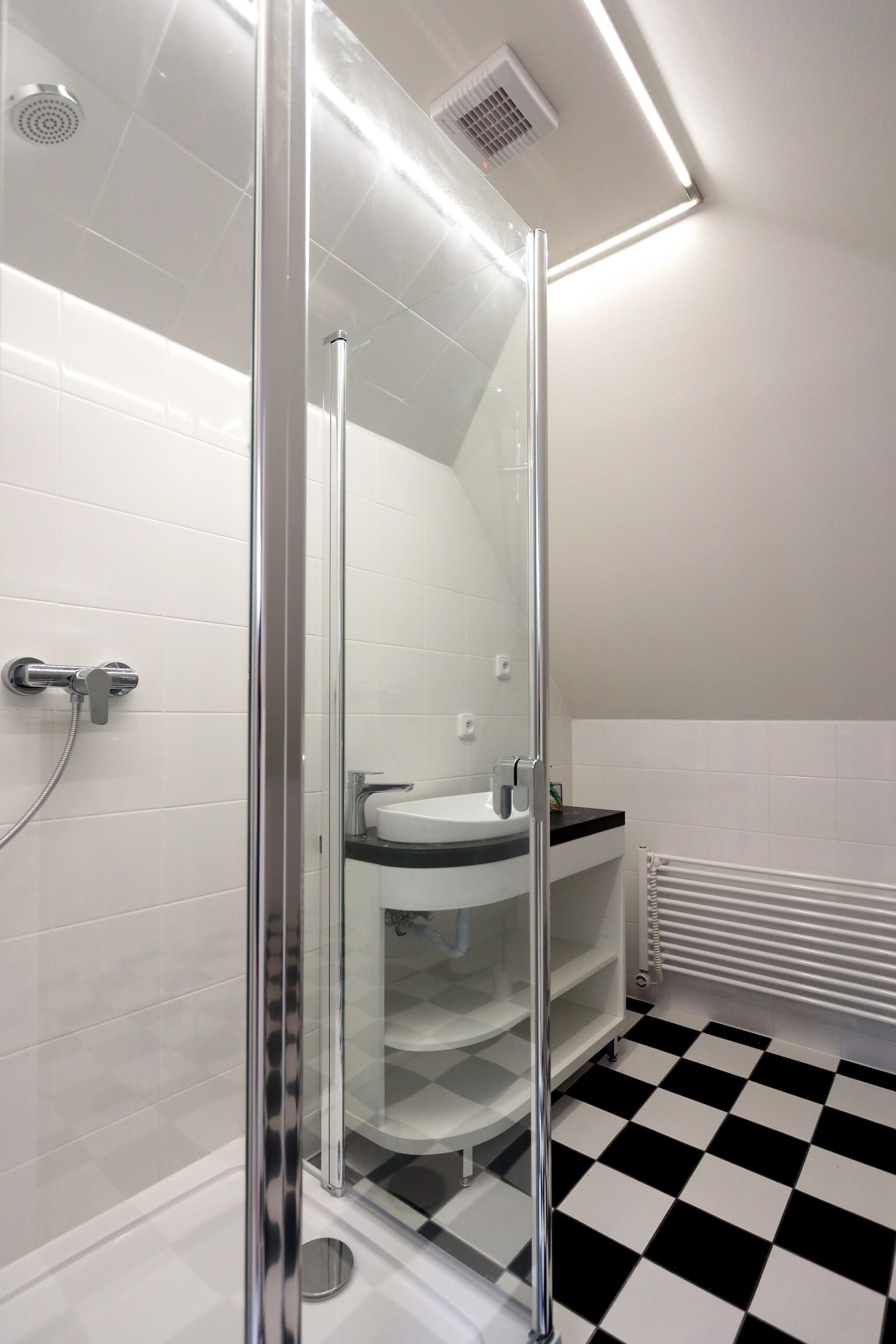 A modern bathroom with a glass shower enclosure, a white sink, and a black and white checkered floor.