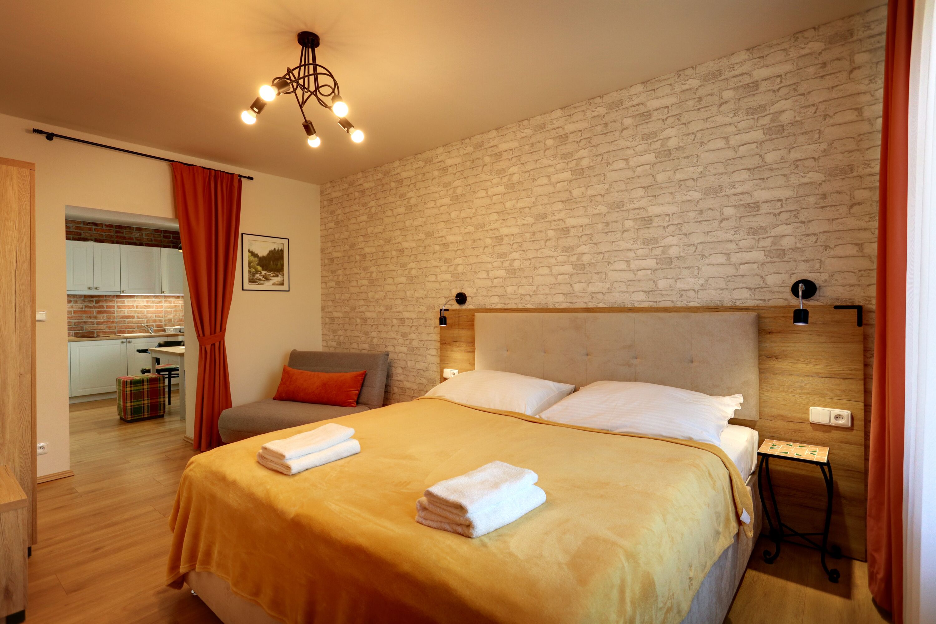 A modern hotel room with a large bed, a wooden headboard, a small table, and a brick wall.