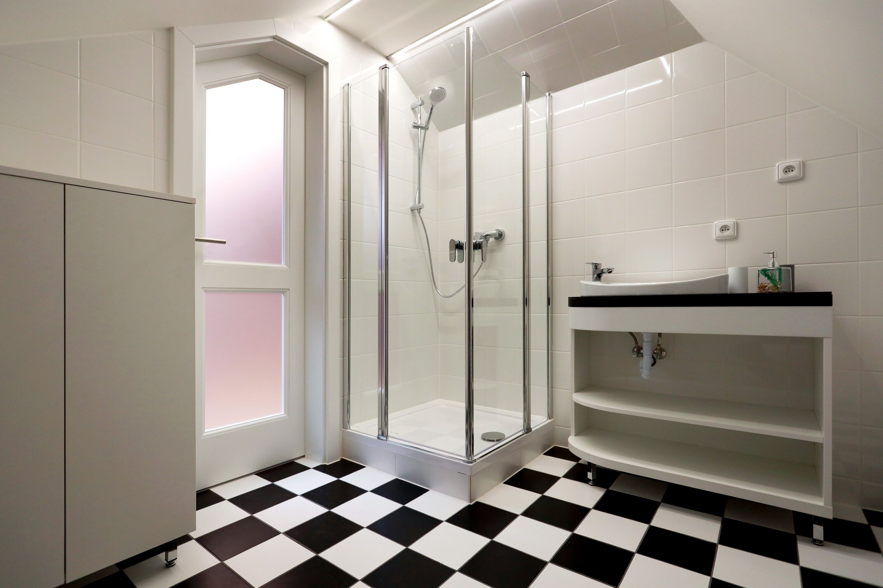 A bathroom with a glass-enclosed shower, a white sink, and a checkered floor.