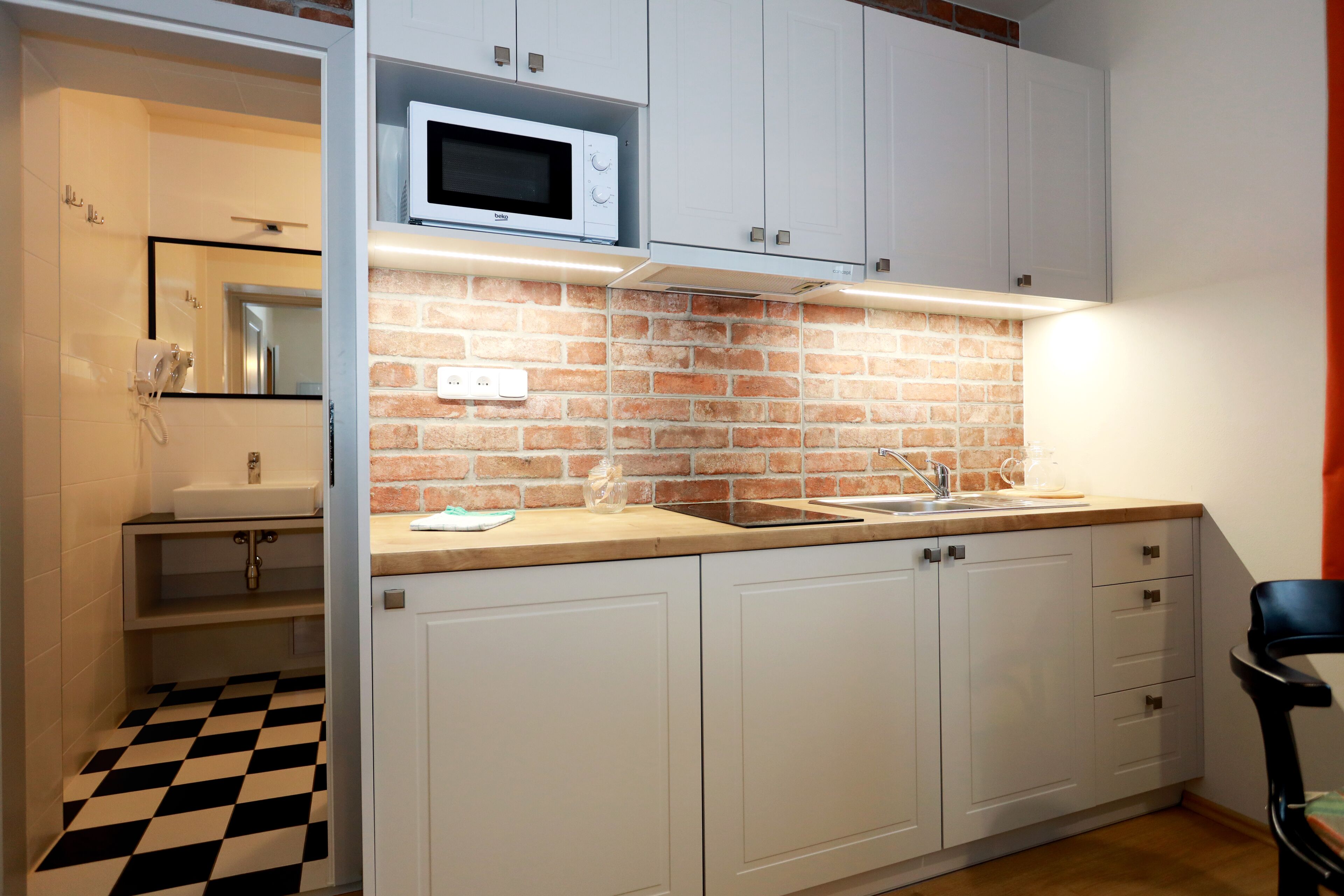 A kitchen with white cabinets, a brick backsplash, a microwave, and a checkered floor.