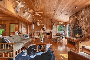 A rustic cabin interior with wooden walls, a stone fireplace, and deer antlers mounted on the ceiling.