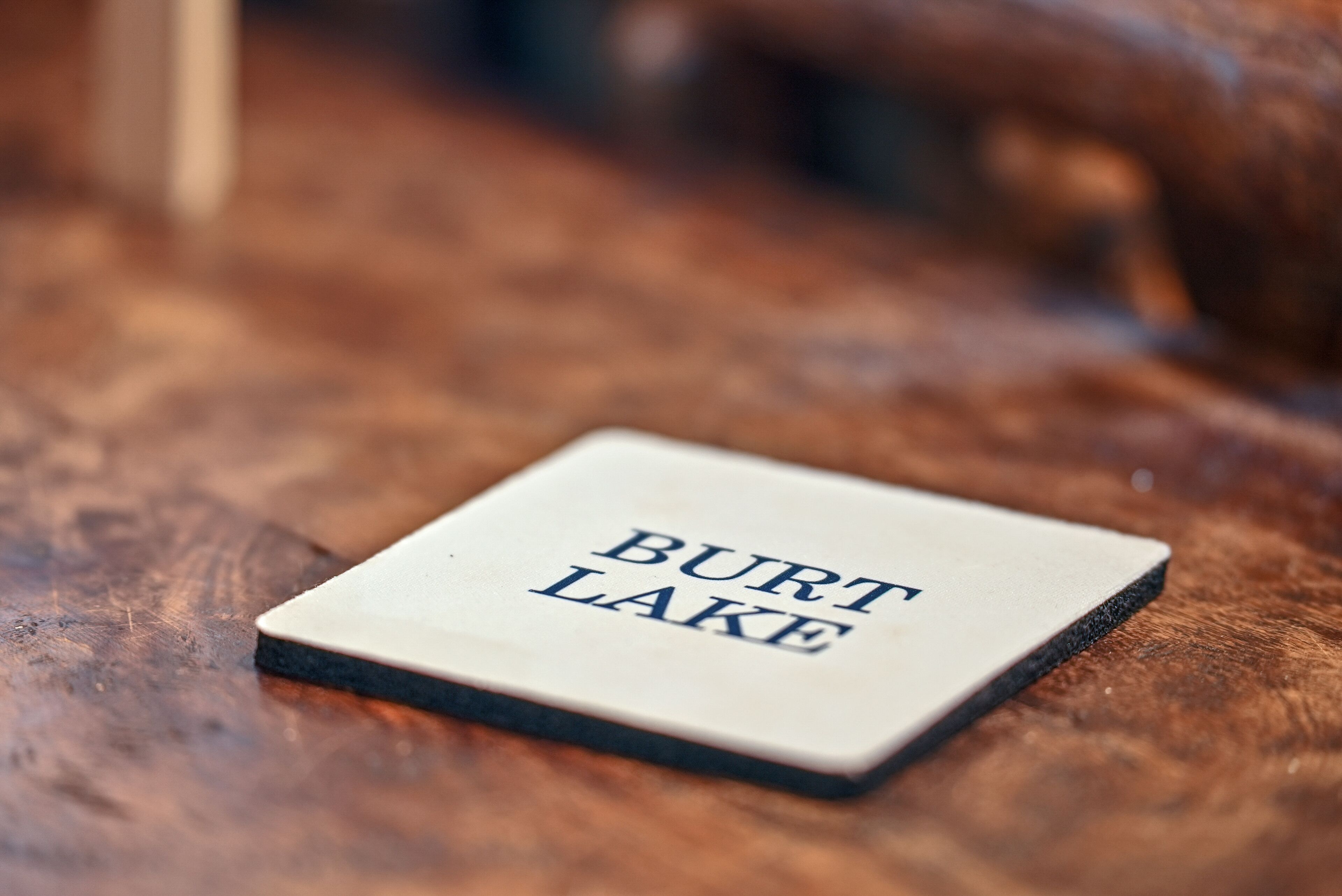A square object with "BURT LAKE" text on it, placed on a wooden surface.