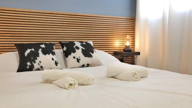 A neatly made bed with white linens and two black and white patterned pillows, a bedside table with a lamp, and a wooden headboard. - Modern & Style Mezquita (Córdoba)