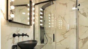 A bathroom with a marble wall, a black sink, a mirror with lights, and a glass shower enclosure. - Modern & Style Mezquita (Córdoba)