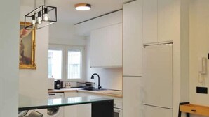 A modern kitchen with a central island, bar stools, a refrigerator, and a wooden shelf. - Modern & Style Mezquita (Córdoba)