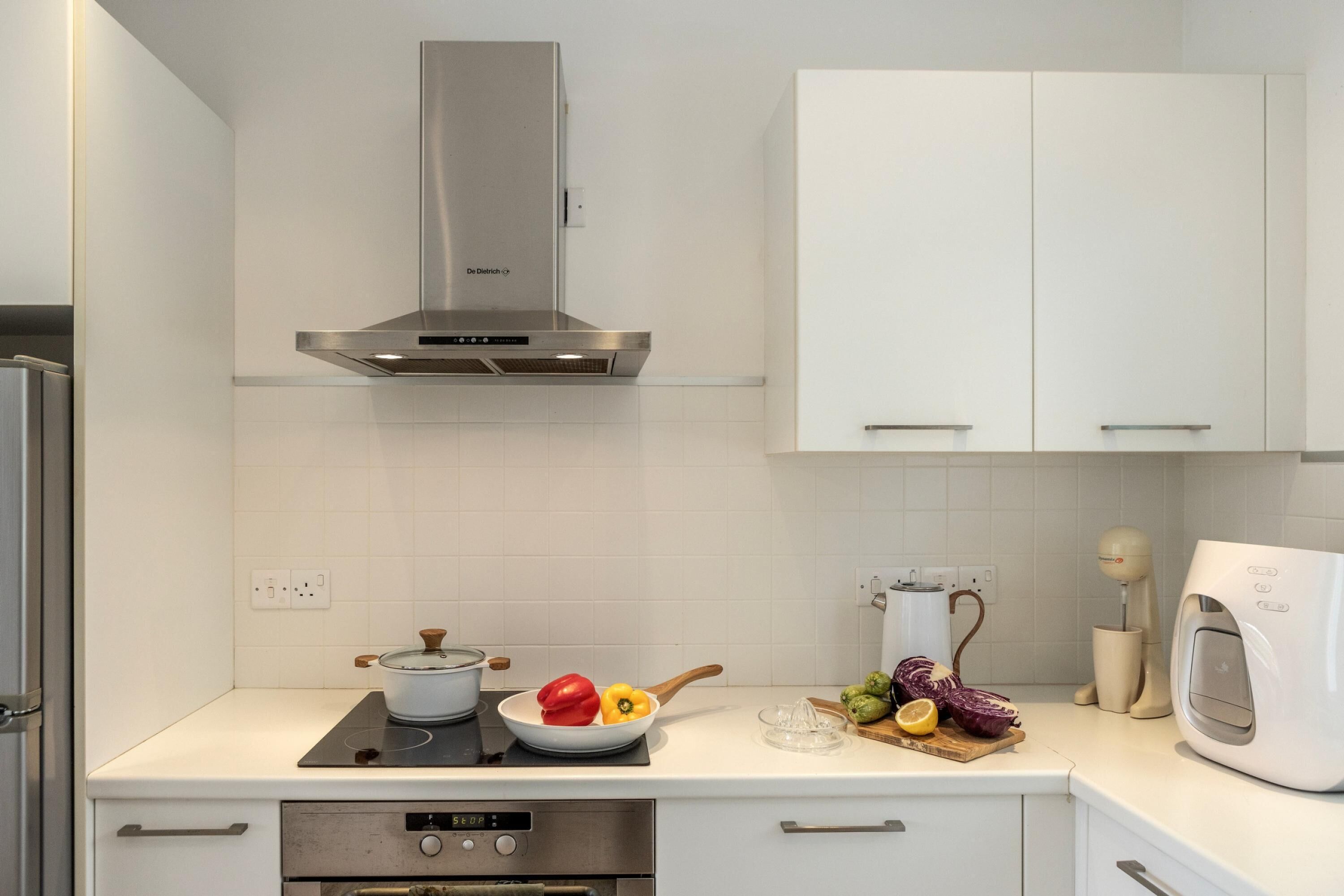 Una cocina moderna con armarios blancos, campana de acero inoxidable, horno empotrado y microondas.