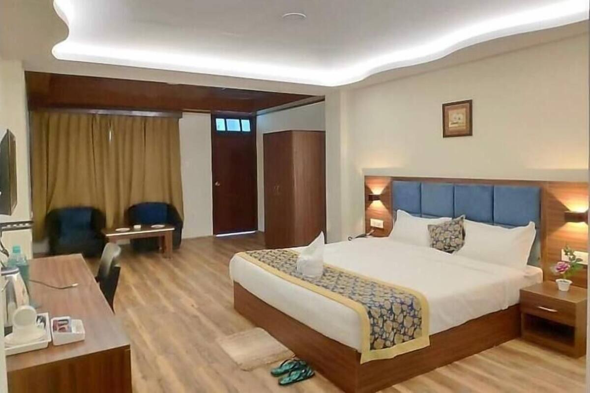 A hotel room with a large bed, a desk with a chair, a wardrobe, and a bathroom visible through an open door.