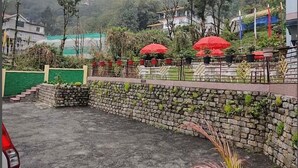 A stone wall with a green gate, a paved area, and red umbrellas.