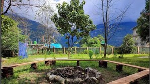 A rustic outdoor area with a fire pit, wooden benches, and a view of mountains.