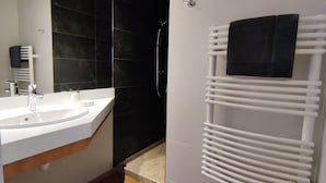 A modern bathroom with a white sink, dark tiles, a shower, and a towel rack.