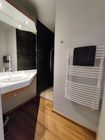 Un baño moderno con un lavamanos blanco, baldosas oscuras, una ducha y un perchero para toallas.