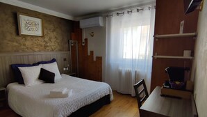 A bedroom with a bed, a desk, a chair, a window with curtains, and a wall-mounted air conditioner.