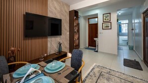 Ein Essbereich mit an der Wand montiertem Fernseher, einer Holzpaneelverkleidung und Blick in ein Badezimmer mit Waschbecken und gerahmten Bildern.