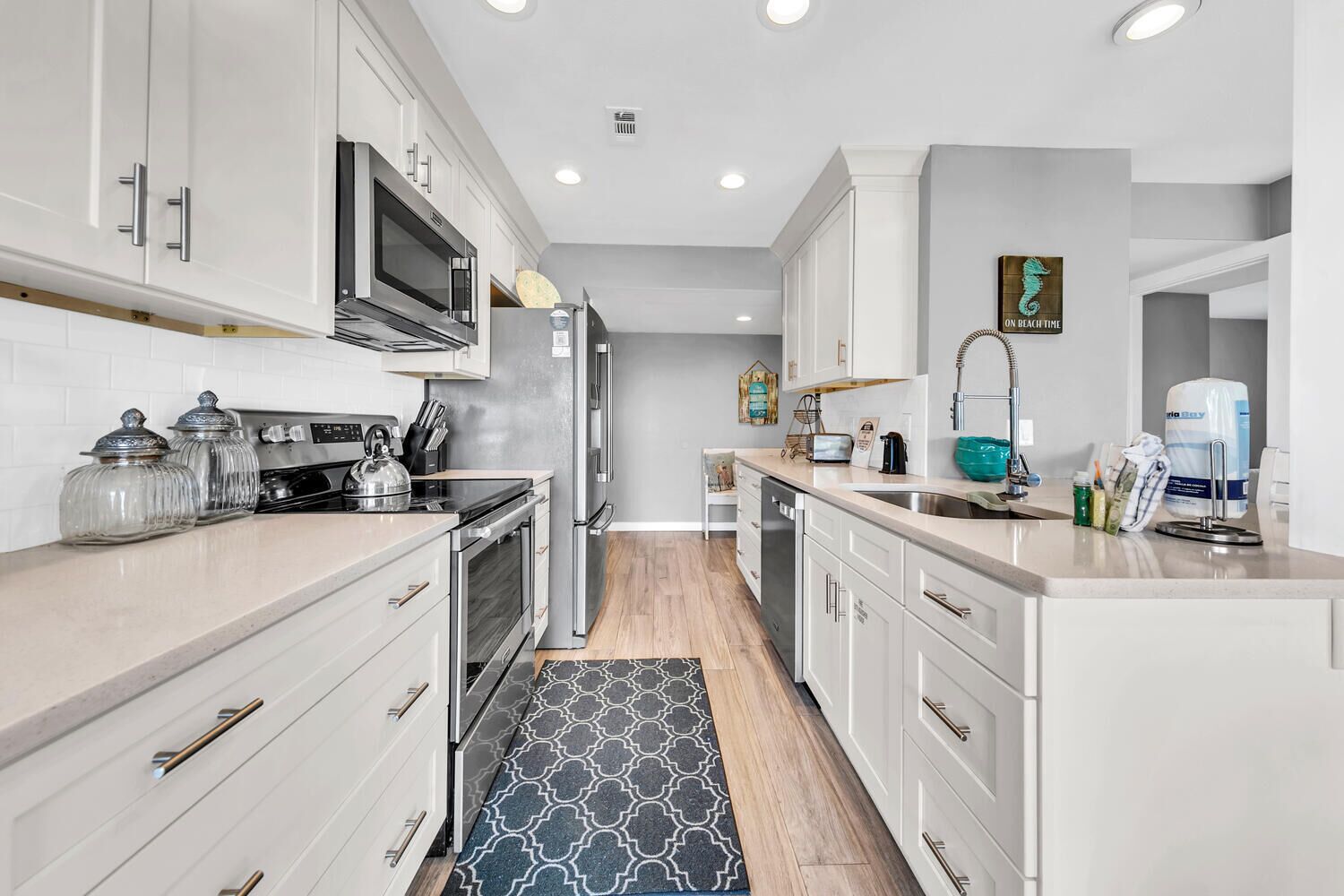 A modern kitchen with white cabinets, stainless steel appliances, and a patterned rug.