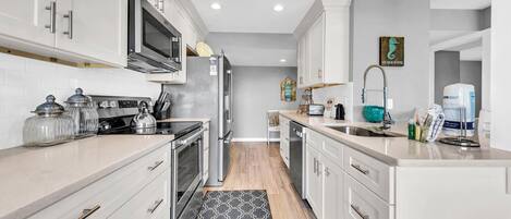 A modern kitchen with white cabinets, stainless steel appliances, and a patterned rug.