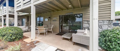 A covered patio area with outdoor furniture, a stone wall, and a glass door entrance.