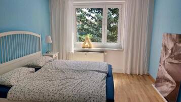 Ein Schlafzimmer mit Bett, Nachttisch, Fenster mit Vorhängen und Heizkörper.