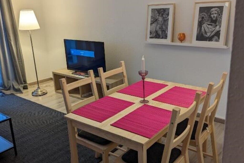 Ein Hotelzimmer mit einem Holztisch, vier Stühlen, einem Fernseher und gerahmten Bildern an der Wand.