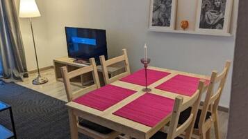 Ein Hotelzimmer mit einem Holztisch, vier Stühlen, einem Fernseher und gerahmten Bildern an der Wand.