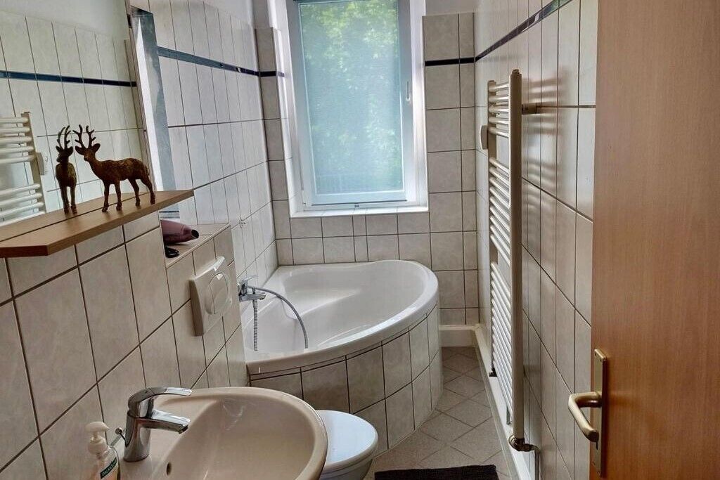 Ein Badezimmer mit einer Badewanne, einem Waschbecken und einer Toilette. Über der Badewanne befindet sich ein Fenster und an der Wand ein Handtuchhalter.