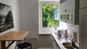Eine kleine Küche mit Fenster, Heizkörper, Spüle und einem Tisch.