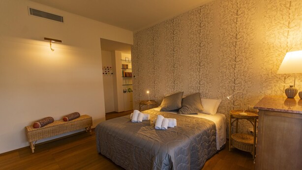 A neatly arranged bedroom with a large bed, bedside tables, a bench, and a lamp.