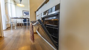 A modern kitchen with a built-in oven, wooden flooring, and a dining area in the background.