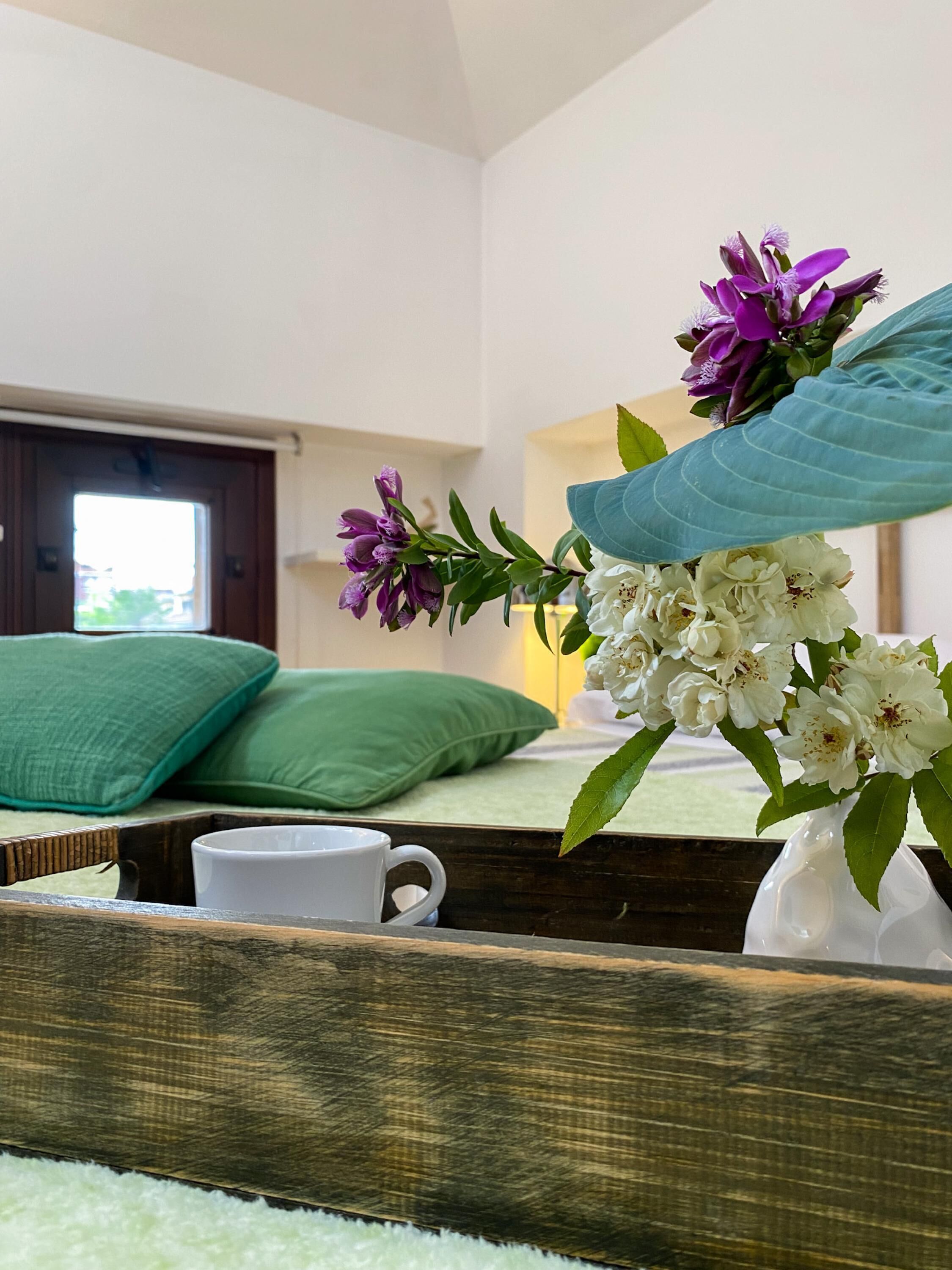 A bedroom with a bed, green pillows, a white mug, and a vase with flowers.