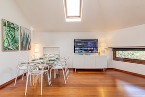 Ein moderner Essraum mit einem Glastisch, weißen Stühlen und einem an der Wand montierten Flachbildfernseher.