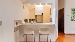 A modern kitchen with a central island, two white bar stools, a refrigerator, and a tiled backsplash. - Il Camino Felice - 201 Autodromo F1 Villa Reale (Monza)