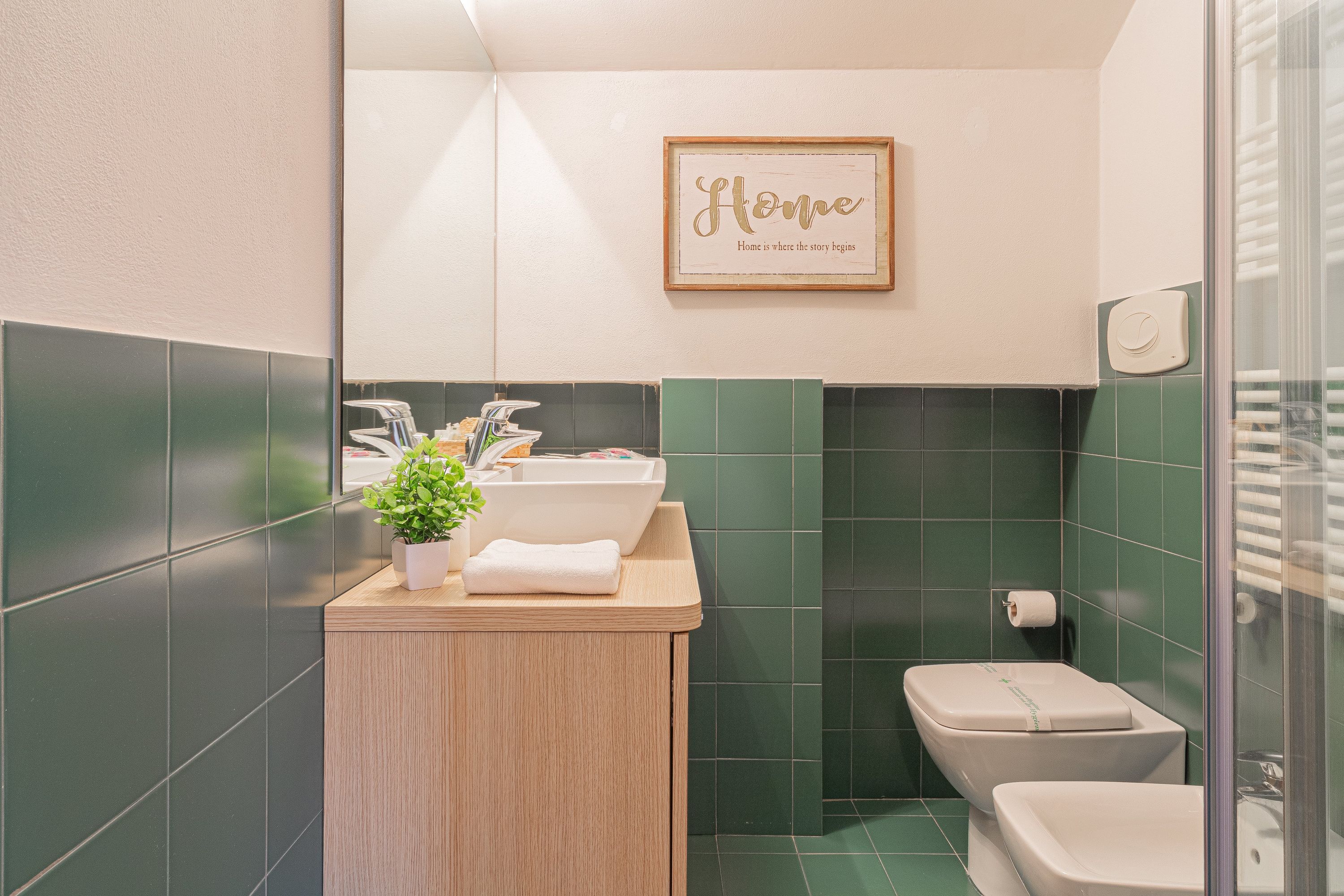 A bathroom with a wooden vanity, a framed inspirational quote, and a green tiled wall.