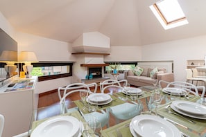 Un coin repas avec une table dressée pour six personnes, un canapé et une cheminée.