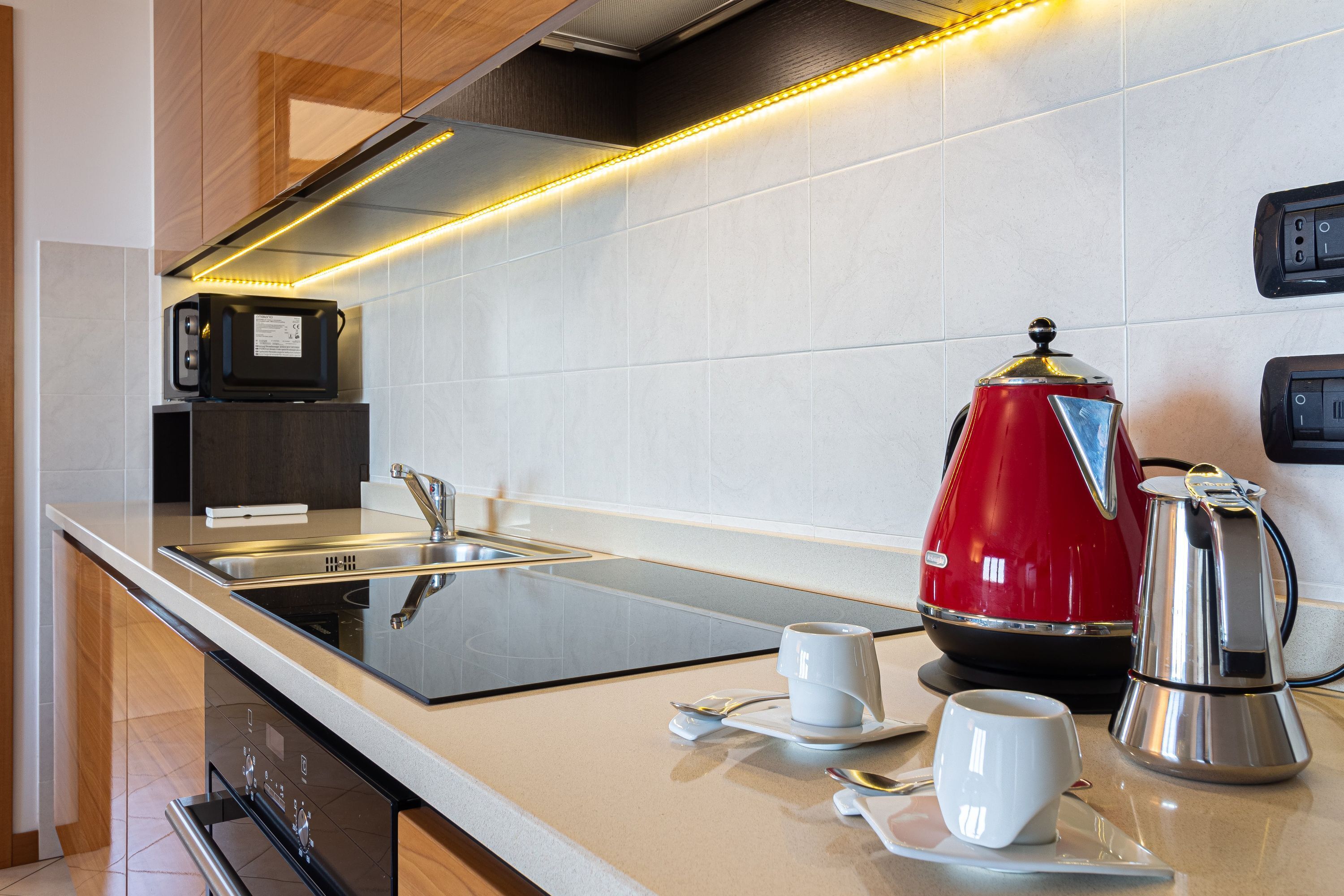 A modern kitchen with a stainless steel sink, a red coffee maker, and a microwave.