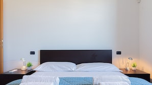 A neatly made bed with white linens, a blue patterned bedspread, and four rolled towels on the bed. There are two bedside tables with lamps and small potted plants. - La Terrazza di Giotto - 501 (Lissone)