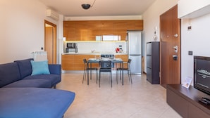 A modern kitchen with wooden cabinets, a dining table with chairs, a sofa, and a TV on a stand. - La Terrazza di Giotto - 501 (Lissone)