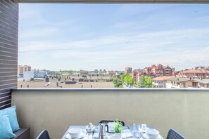 A balcony with a table set for dining, overlooking a residential area with various buildings.