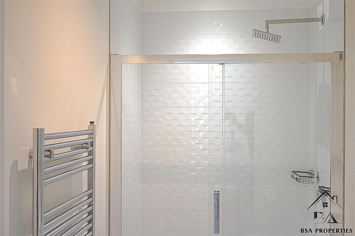 Un baño con cabina de ducha de vidrio, un perchero y un cabezal de ducha.
