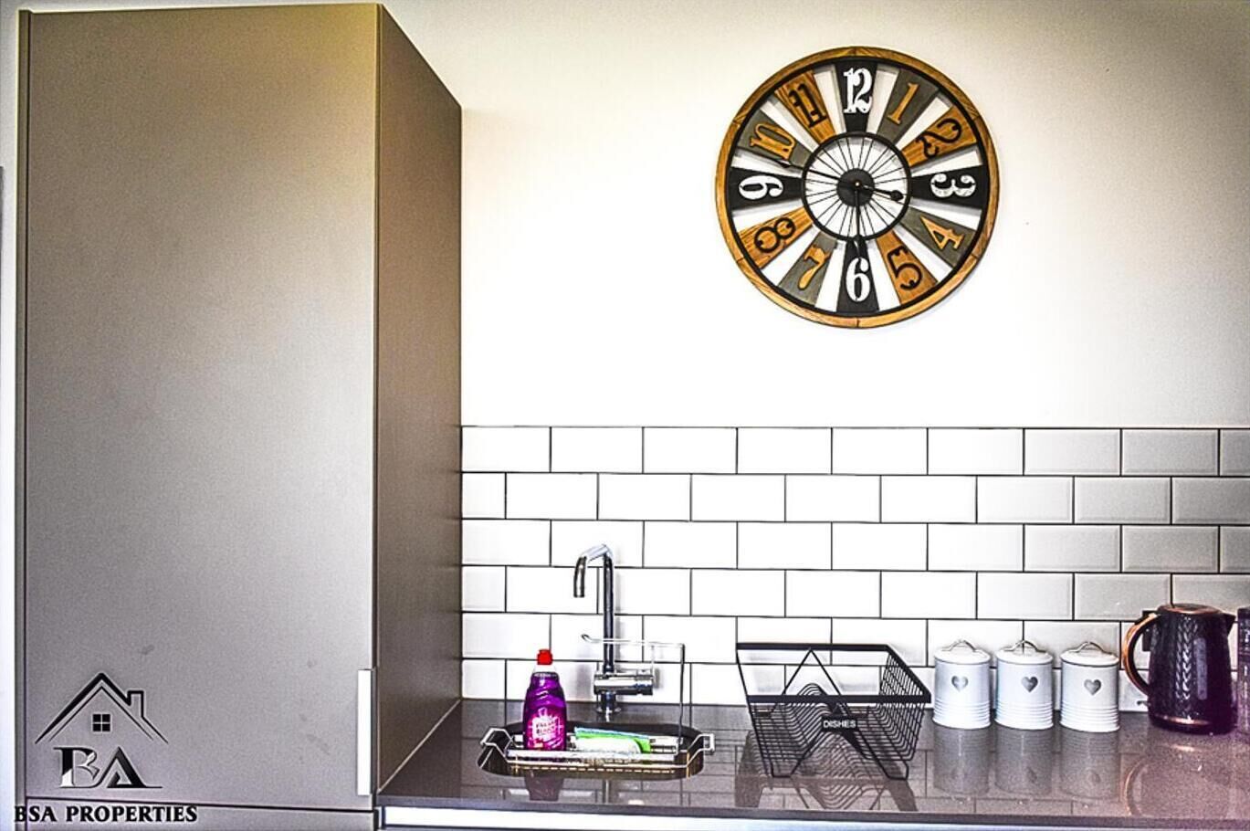 Uma cozinha com design moderno, apresentando um painel de azulejos brancos, uma pia de aço inoxidável e um relógio redondo na parede.