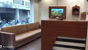 Un'area reception con una scrivania in legno, una televisione montata sopra, un divano e una scala che conduce a un piano superiore.