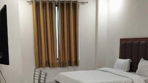 Una camera d'albergo con un letto, una scrivania, una sedia e una finestra con tende.