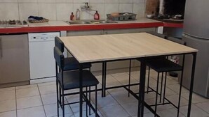 A compact kitchen with a wooden table and two chairs, a sink, and a refrigerator. - Coeur de Fitou : Maison de Village Atypique (Fitou)