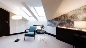 A modern room with a skylight, a blue chair, a small table with a vase of flowers, and a wall with a leaf pattern. - Green Krupnicza (Kraków)