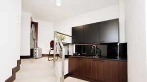 A modern kitchen with dark wooden cabinets, a black countertop, and a large flat-screen TV above the sink. - Green Krupnicza (Kraków)