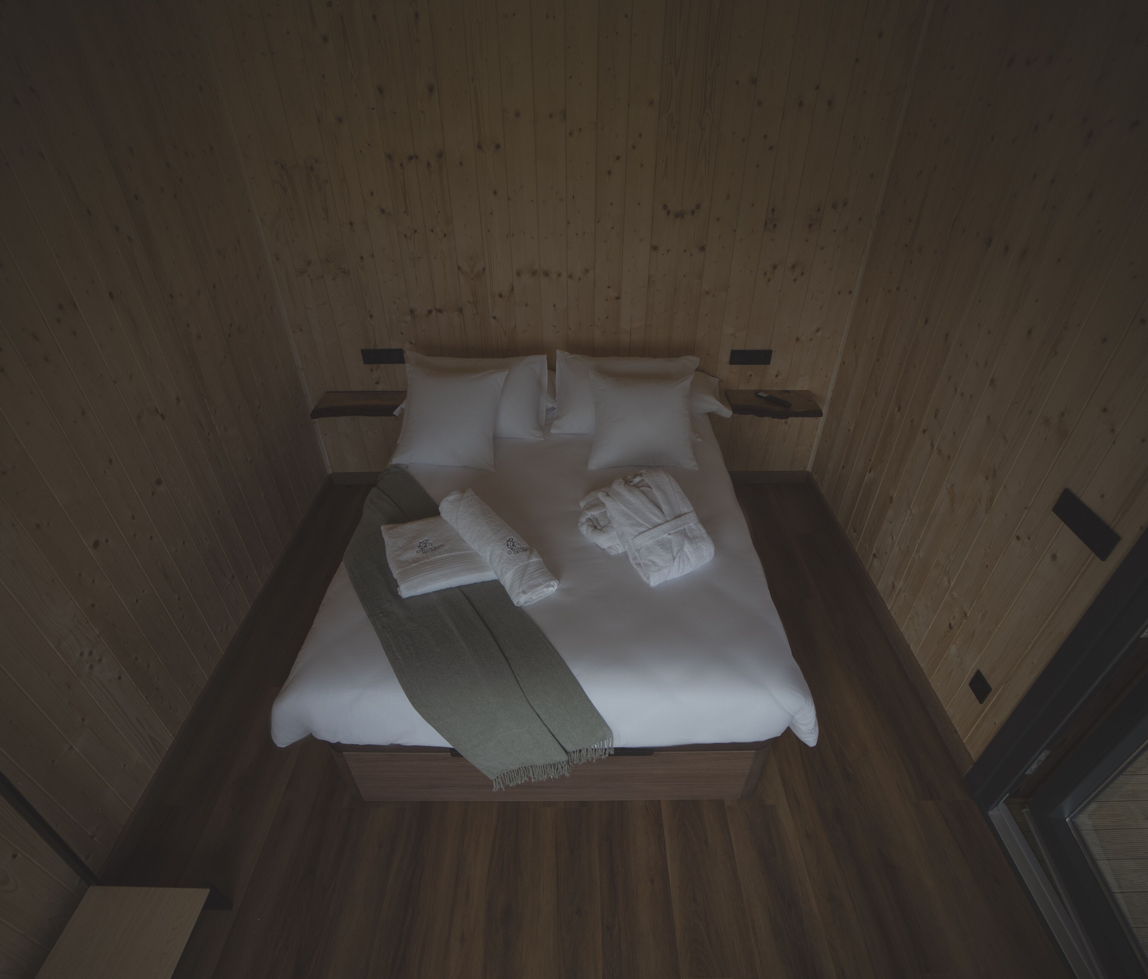 Una habitación con paneles de madera, una cama, almohadas y toallas.