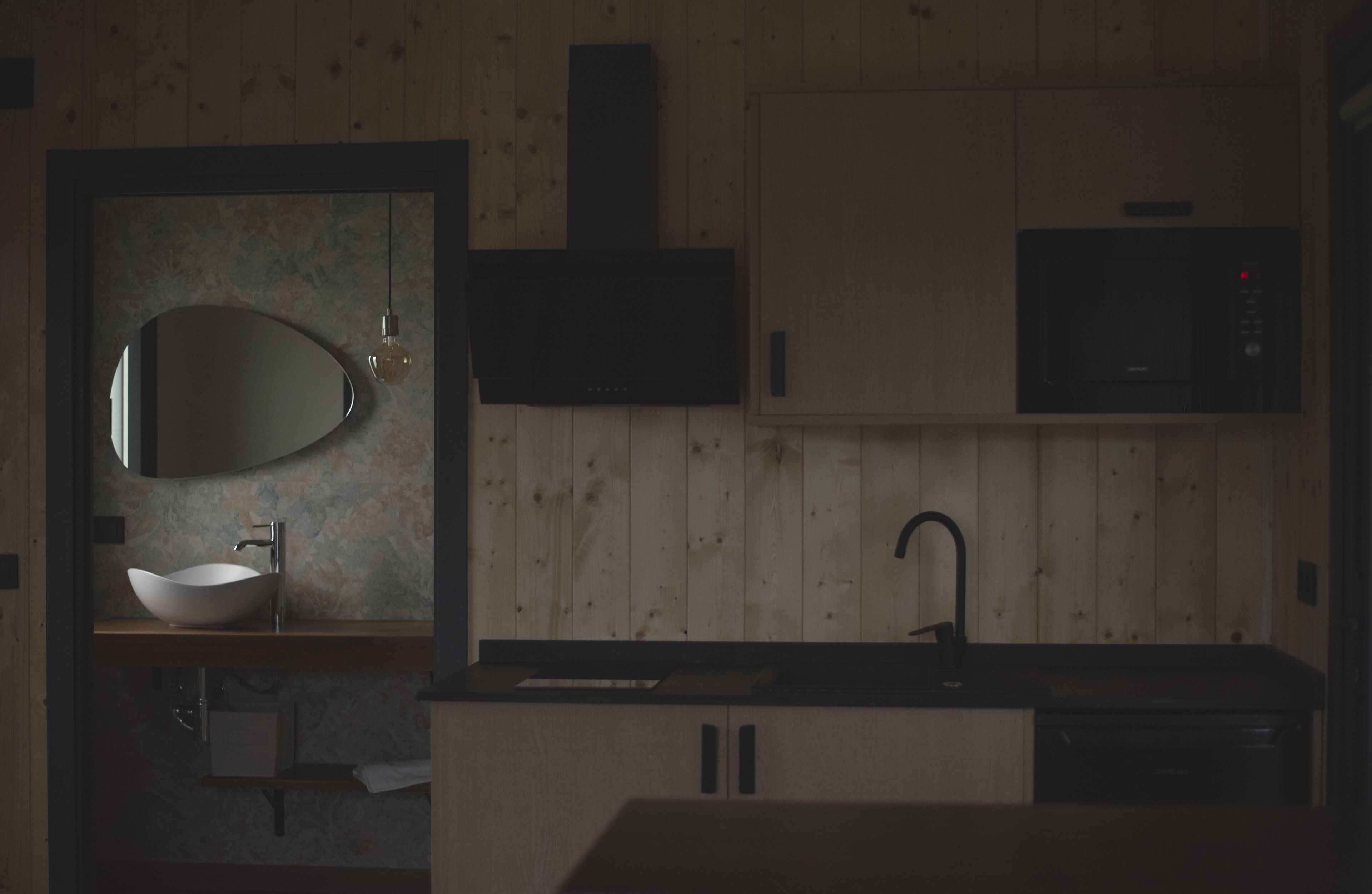 A modern kitchen with a wooden finish, a built-in sink, a microwave, and a large mirror.